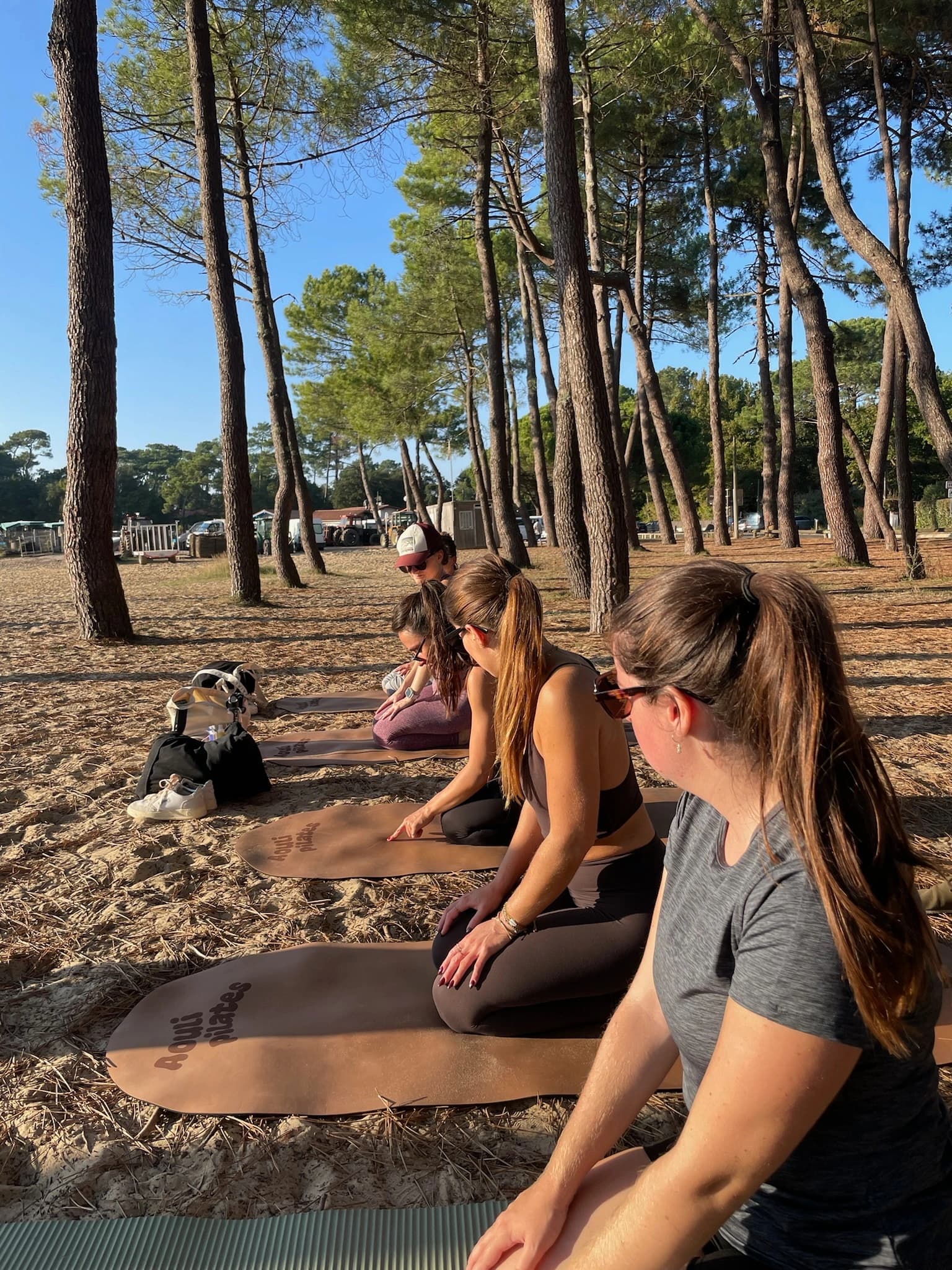 Women sitting on Pilates mats among the pines during a morning session on the sand