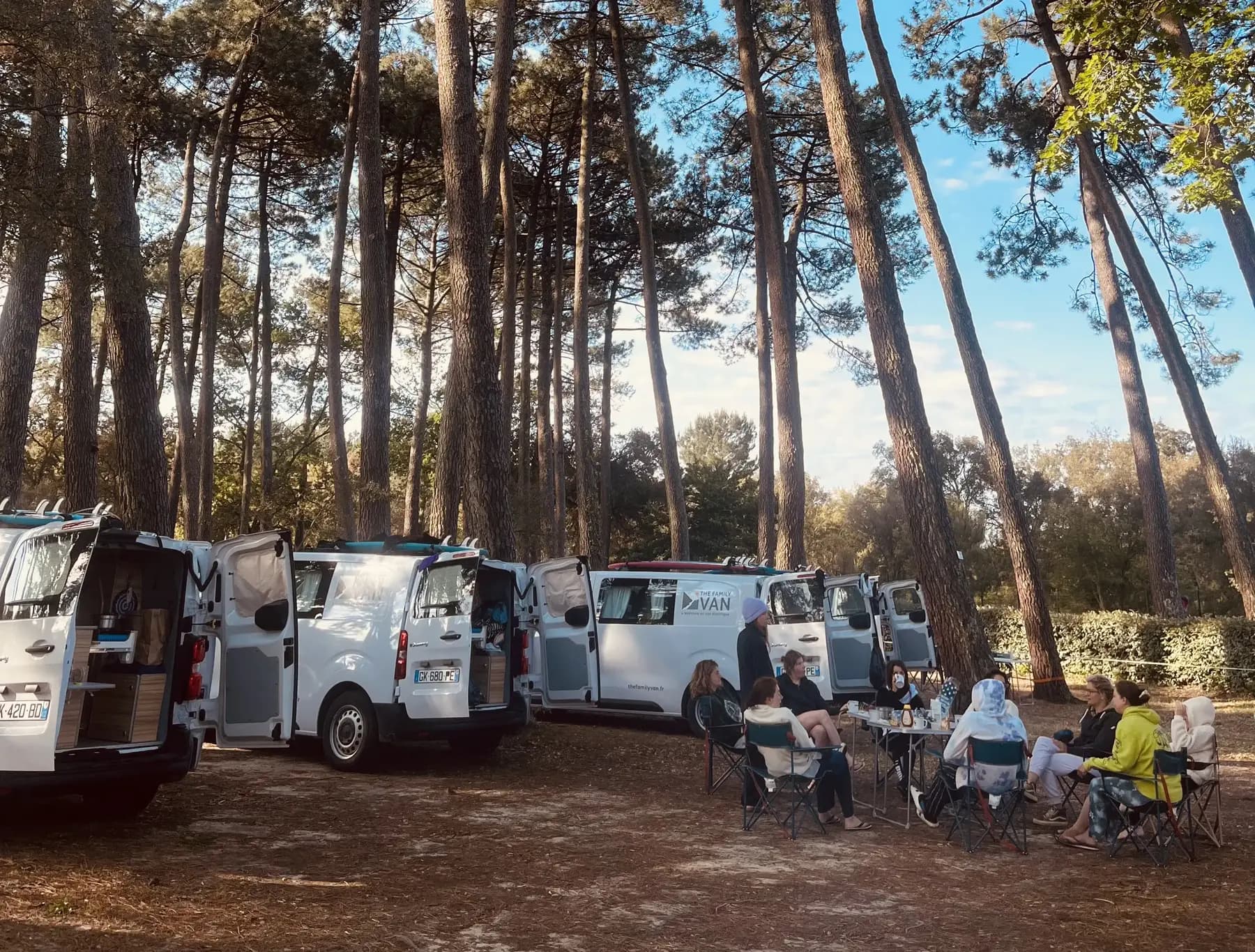 Four campervans pitched in a circle under the pines, the group sitting at a table nearby