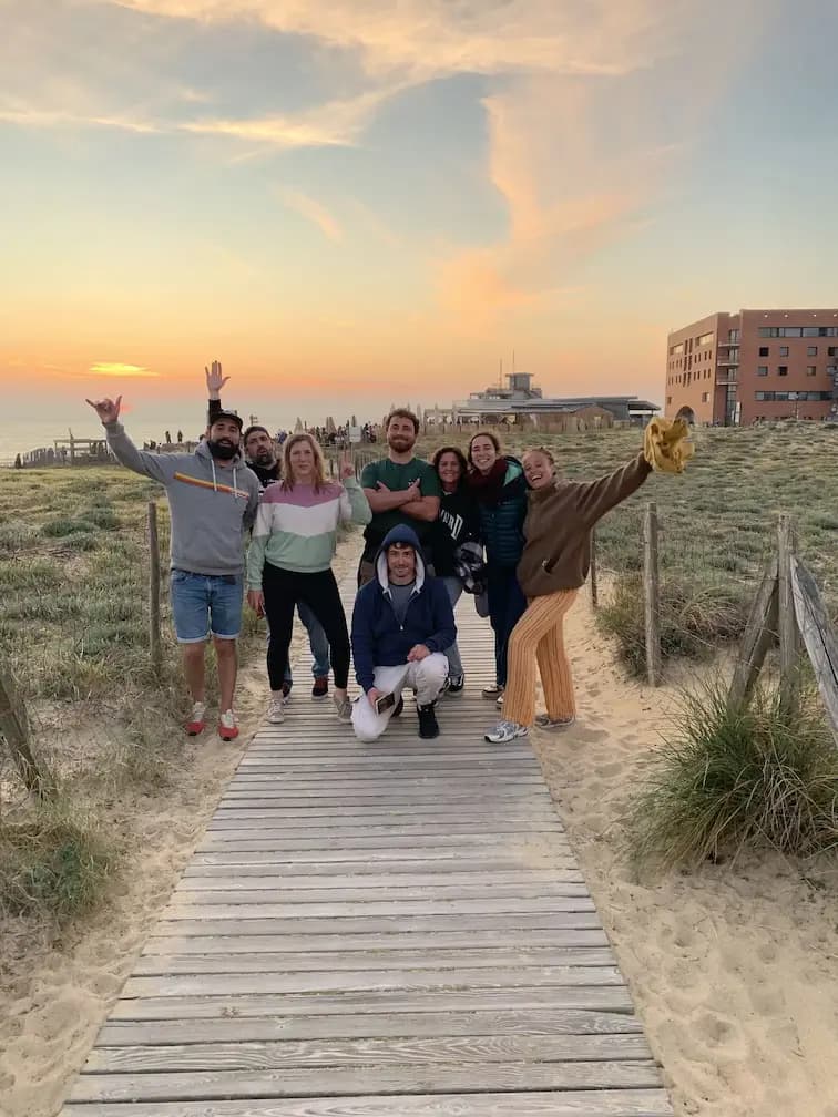A cheerful group posing with arms raised on a boardwalk through the dunes at sunset