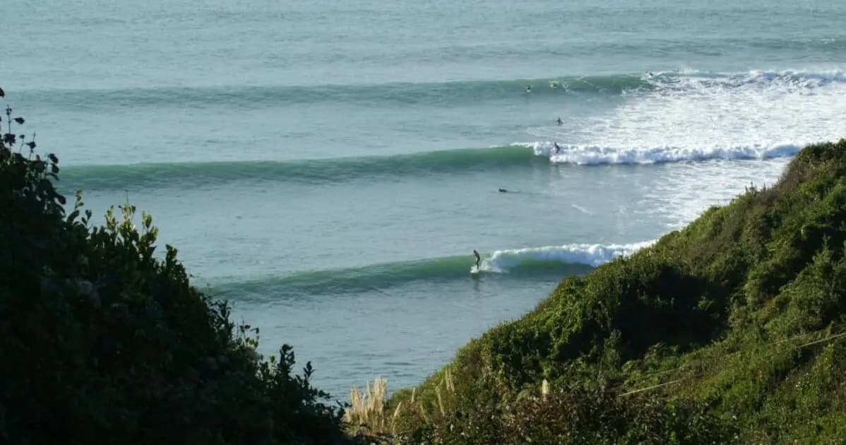 Even lines of waves framed by two green hillsides, a few surfers waiting at the peak