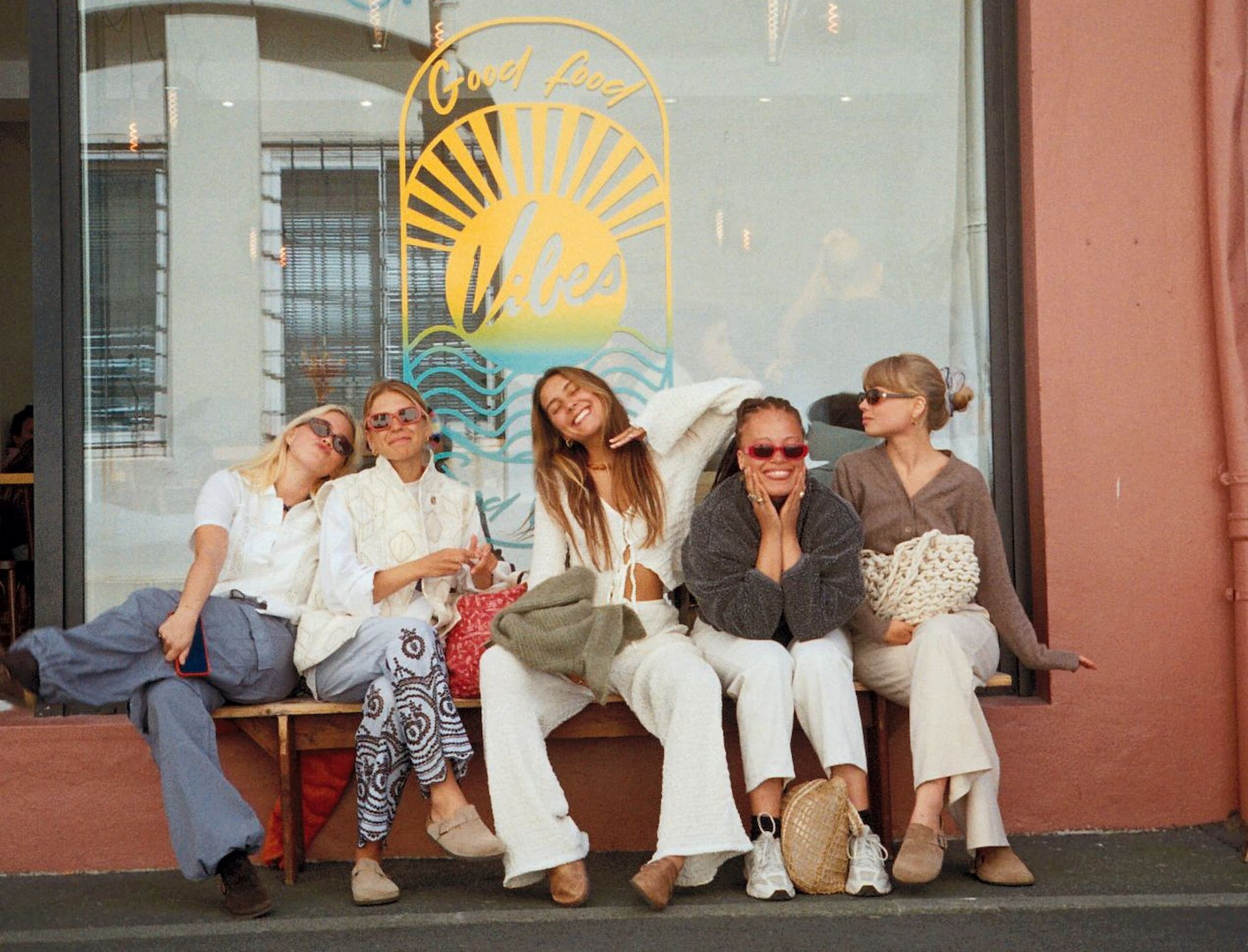 Five friends sitting on a bench in front of a cafe window in Biarritz, dressed in white