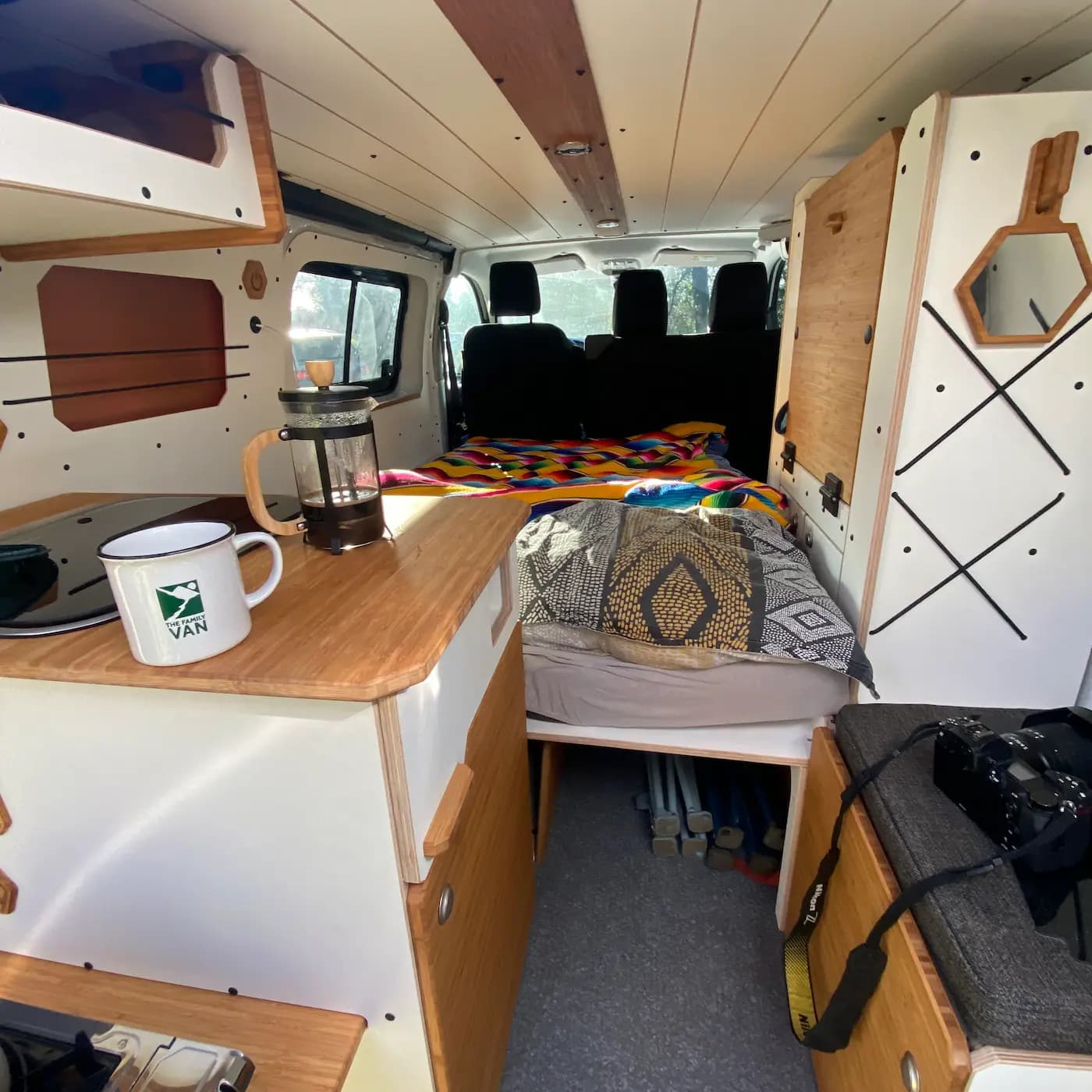 Inside an electric campervan with a wooden worktop, cafetière and made-up sleeping area