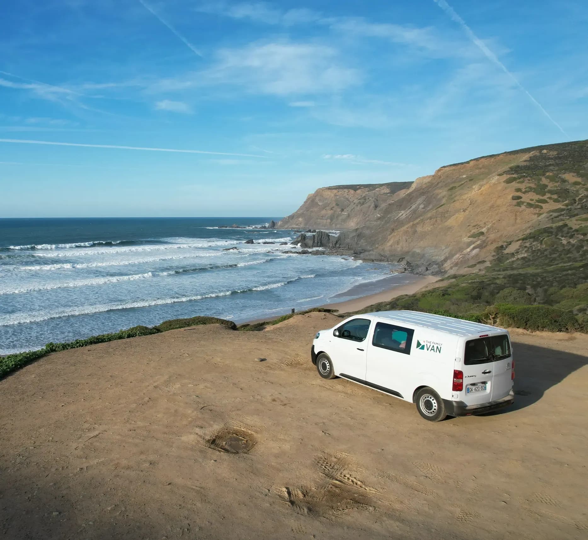 Campervan parked on a clifftop headland above a beach worked by long lines of rollers