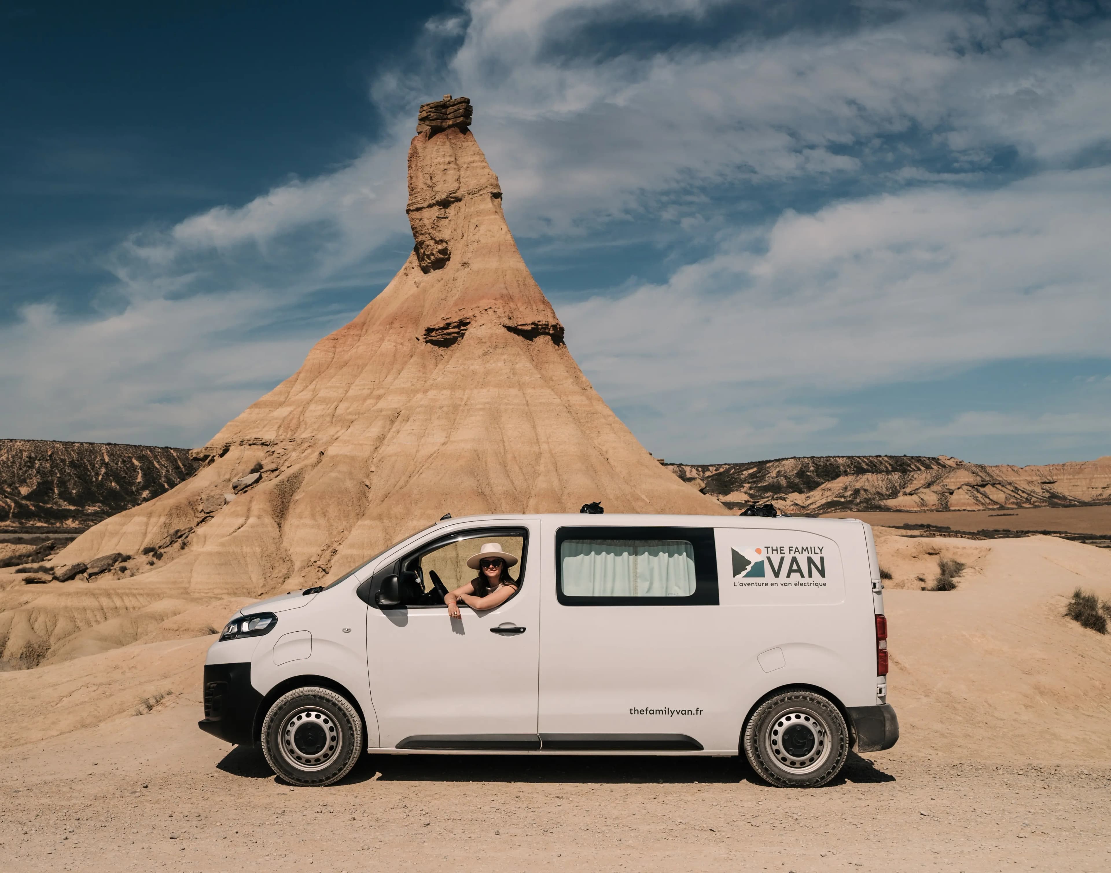 The Family Van campervan parked beneath a Bardenas desert rock spire, a customer at the window