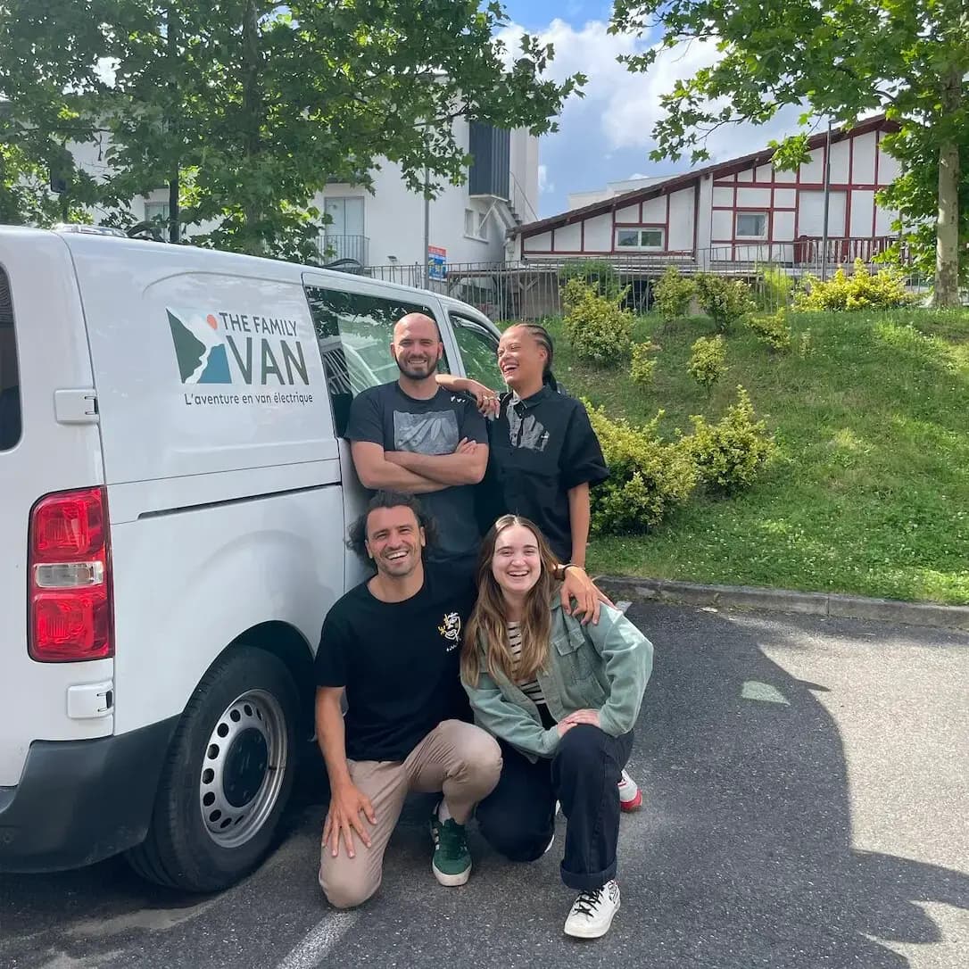 Four team members posing and laughing in front of a campervan badged The Family Van