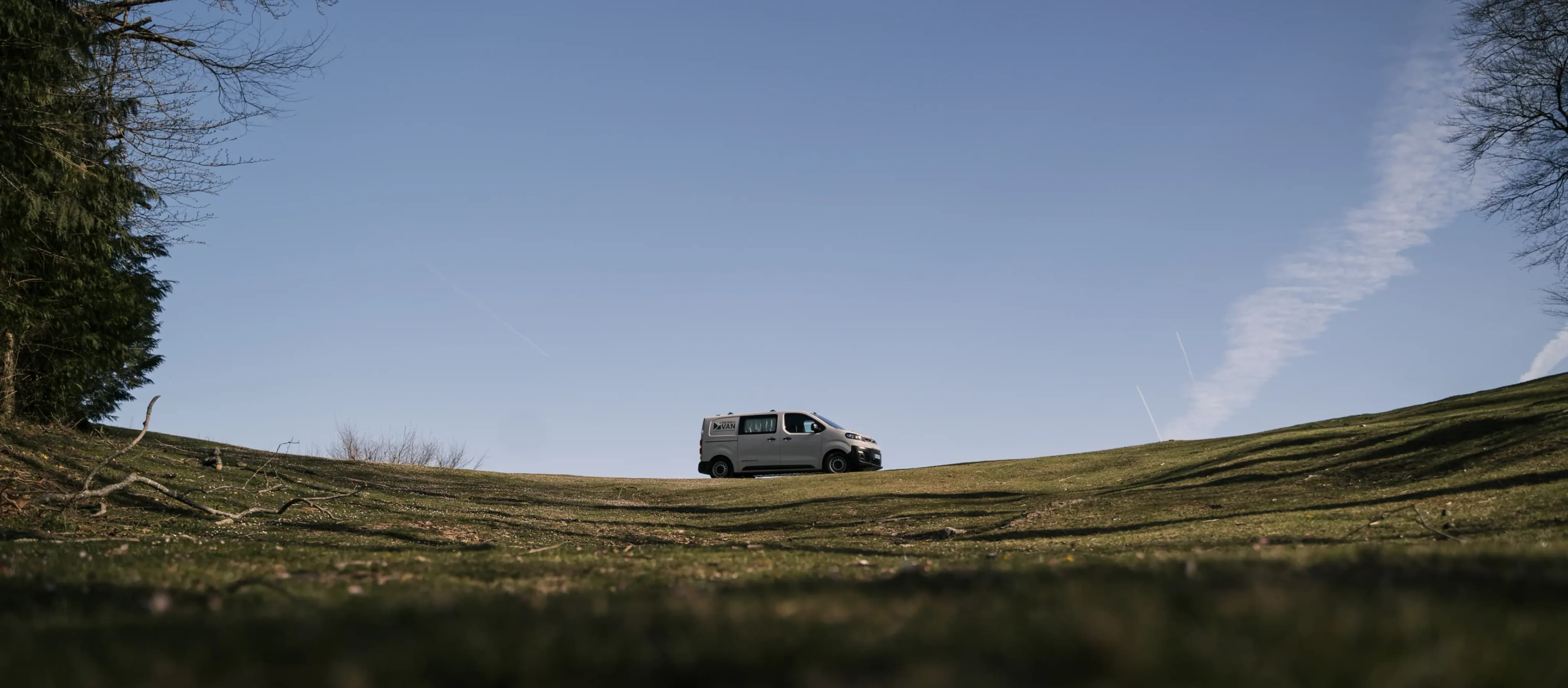 A lone campervan on a grassy ridge under a wide blue sky, photographed from ground level