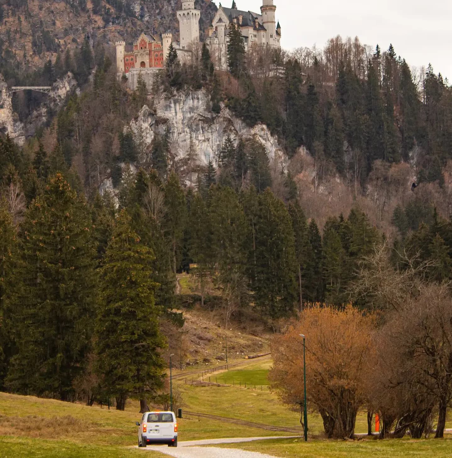 White van on a country lane at the foot of a wooded hill crowned by a fairy-tale castle