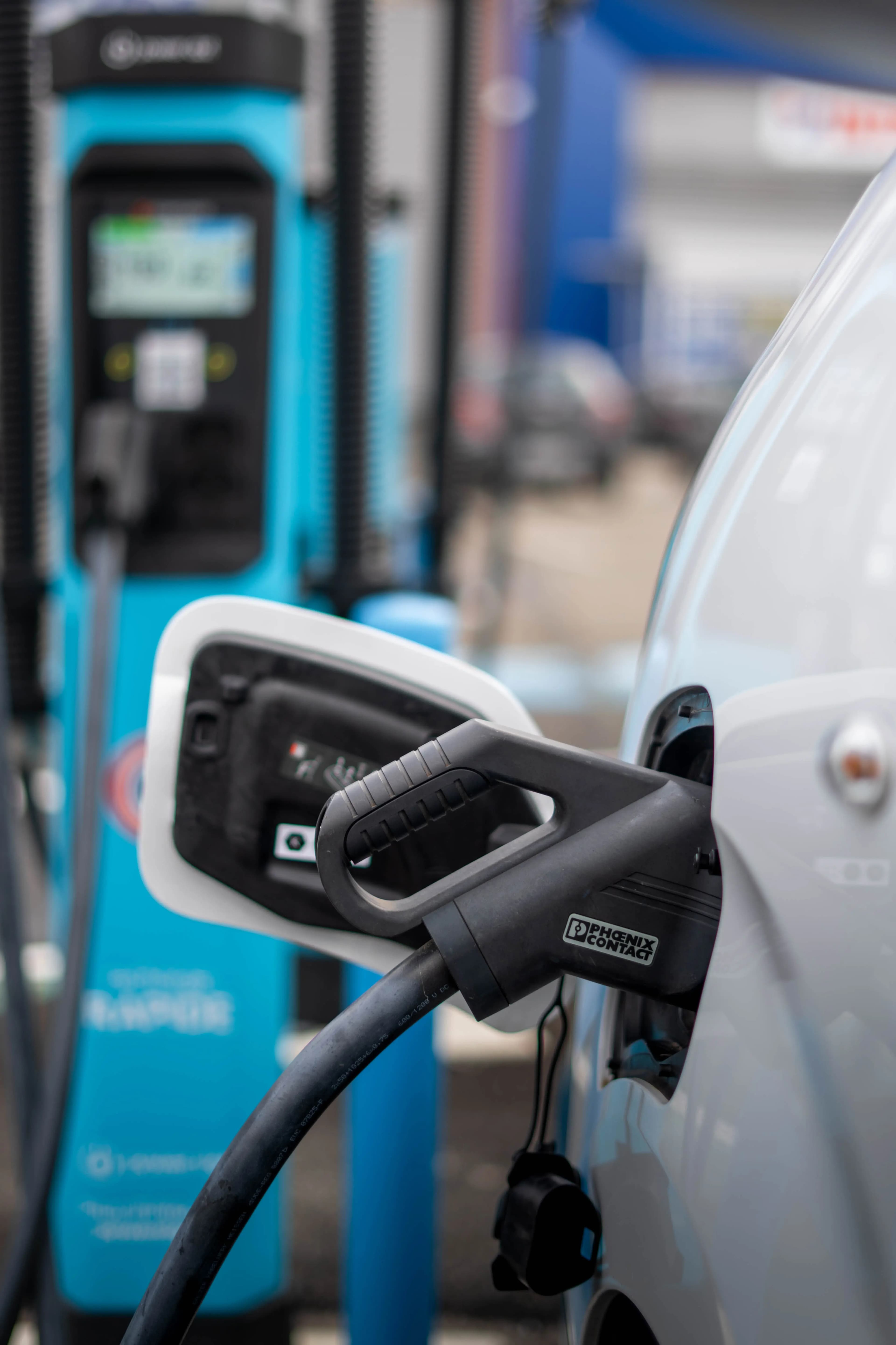 Cable plugged into the charging flap of an electric van, a blue charging point behind