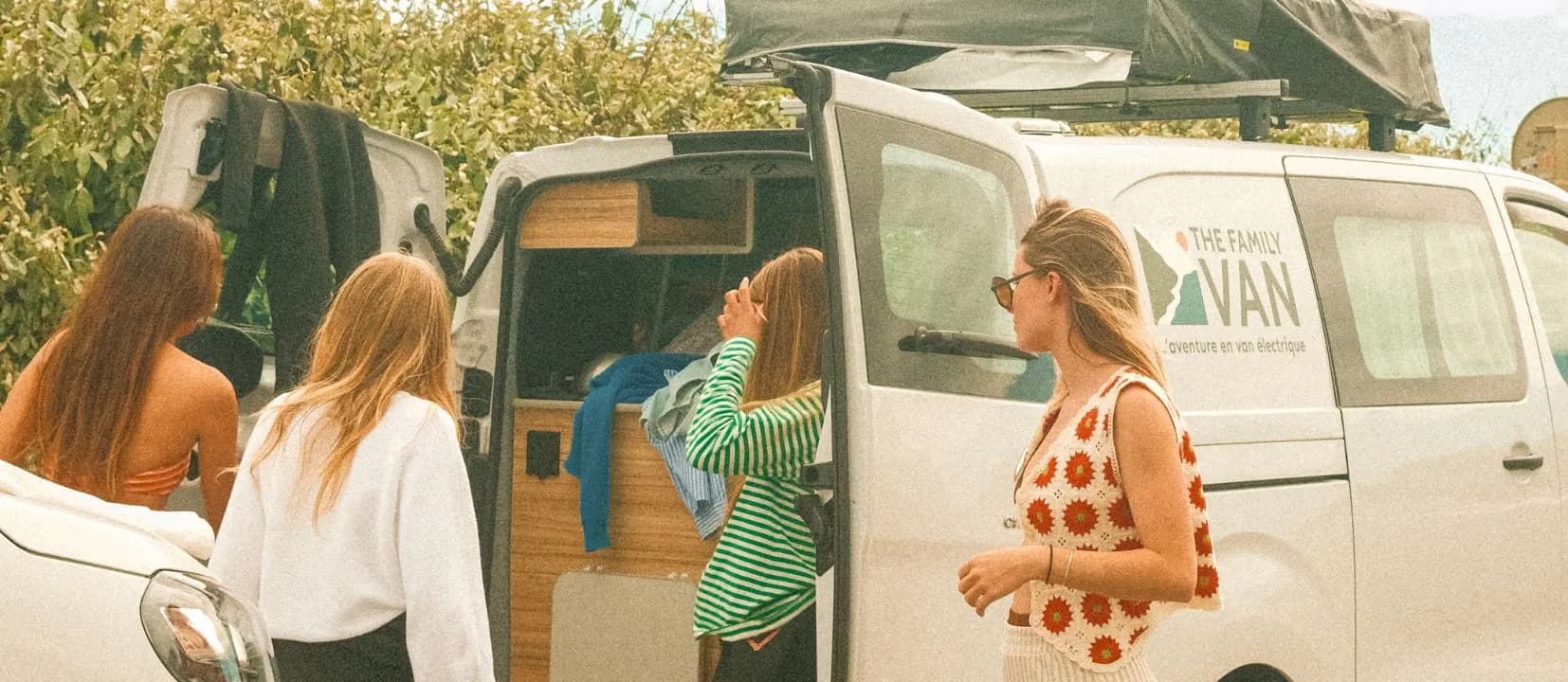 Four women getting their things ready around a white campervan with its roof tent up