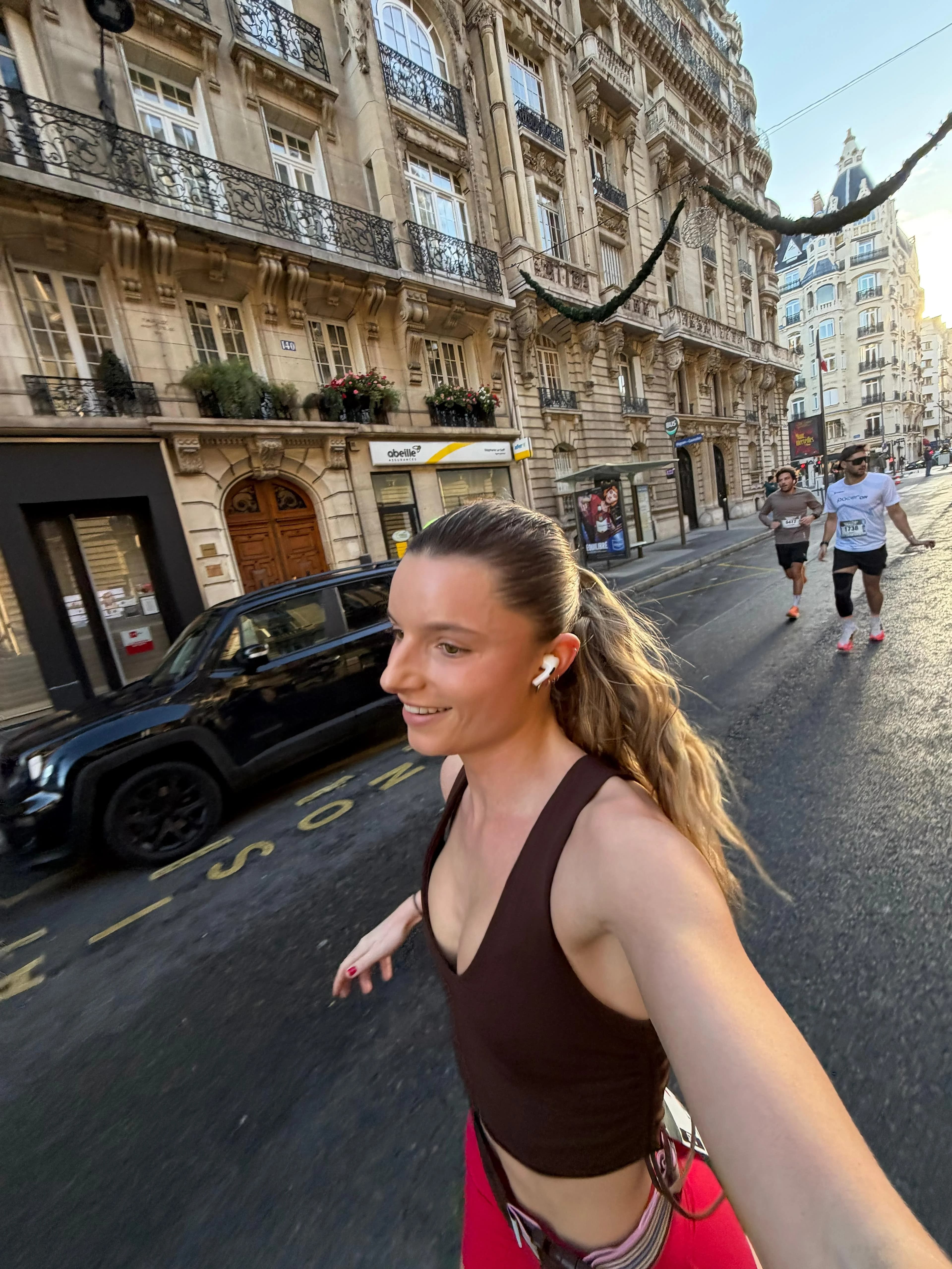 Smiling runner taking a selfie in a Haussmann-style street, two runners following behind