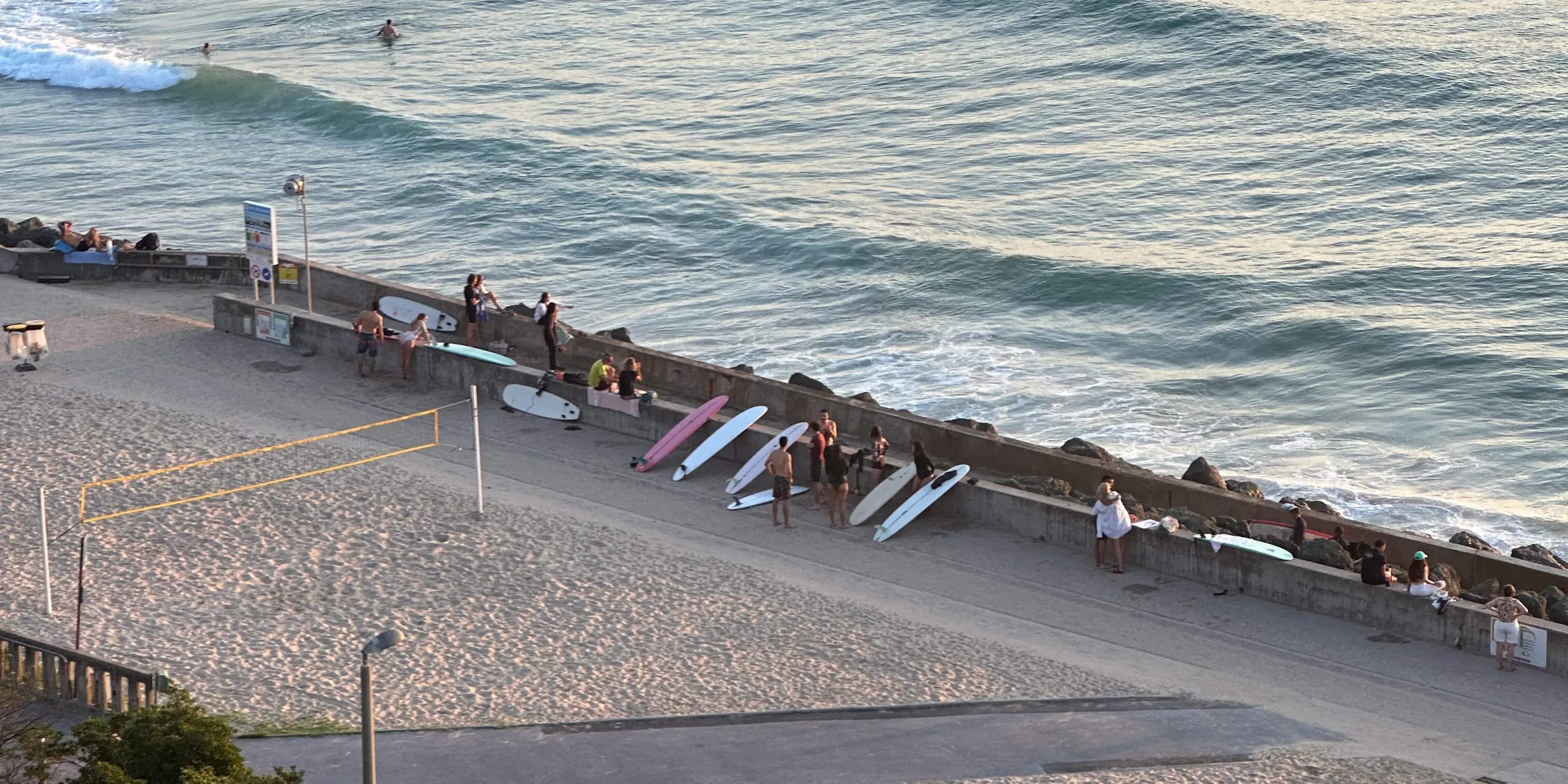 Surfers and boards lined up along the sea wall of a Biarritz beach in the evening light