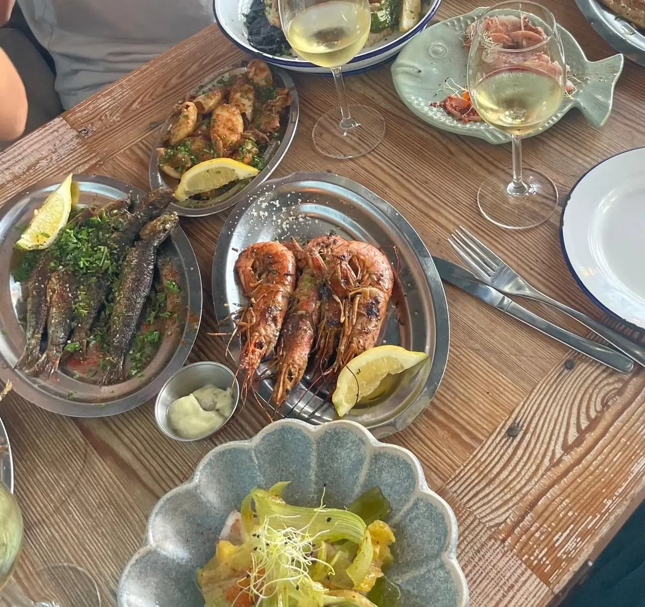 Restaurant table spread with grilled sardines, prawns and squid, glasses of white wine