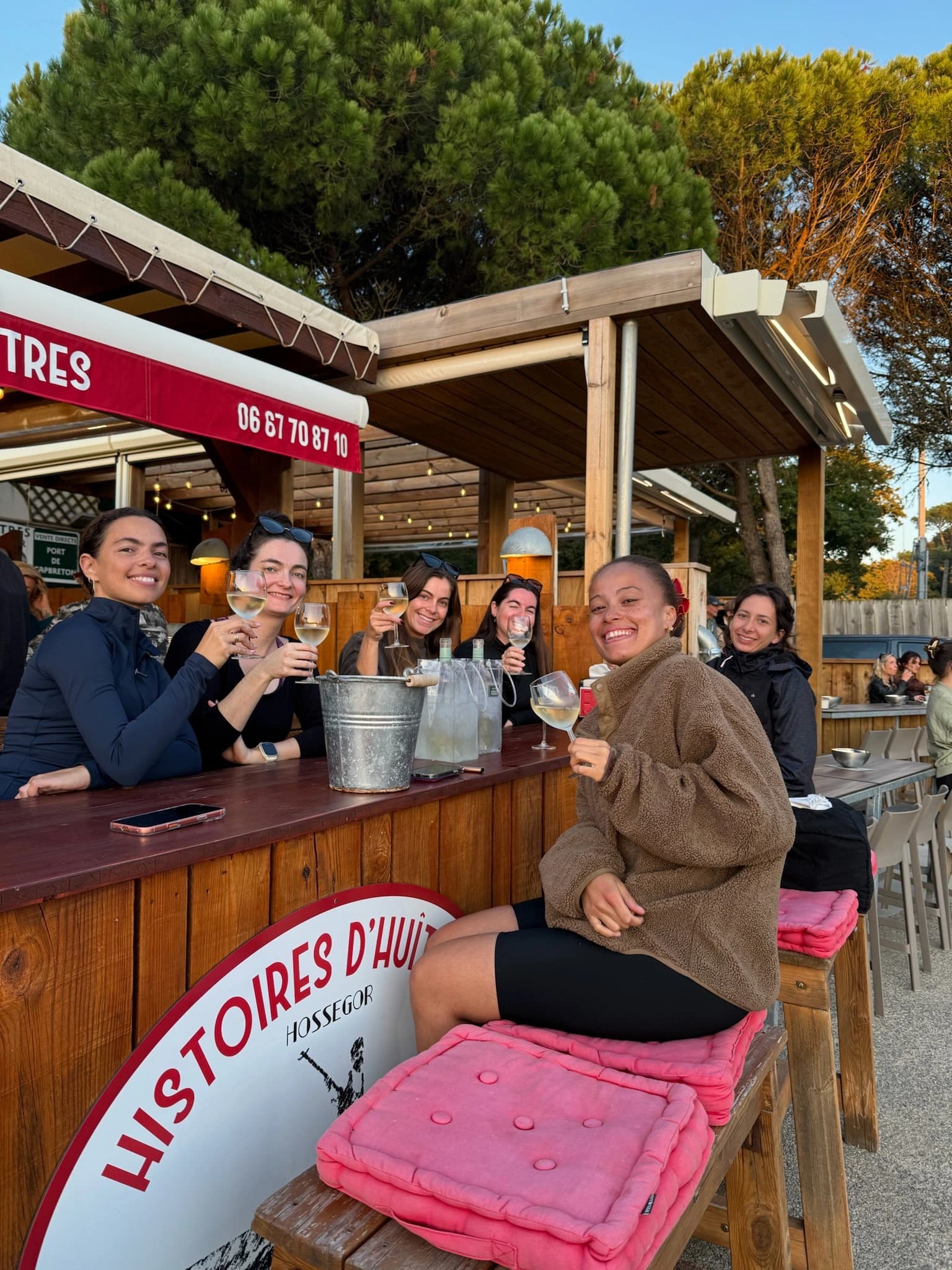 Group of women raising glasses of white wine at the counter of an oyster shack in Hossegor