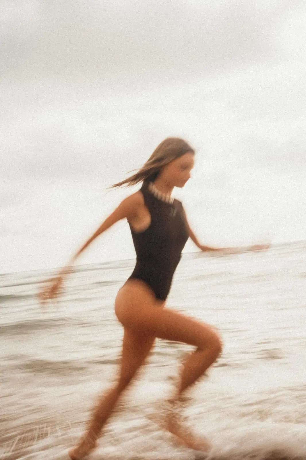 A woman in a black swimsuit running through the surf, caught in a soft motion blur