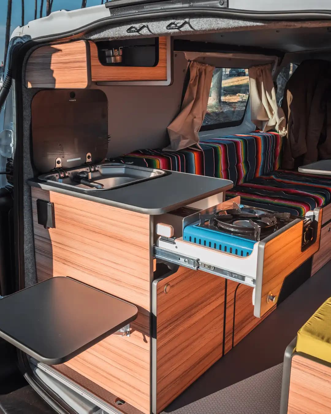 Fitted campervan kitchen: sink, slide-out hob, folding table and a striped bench seat