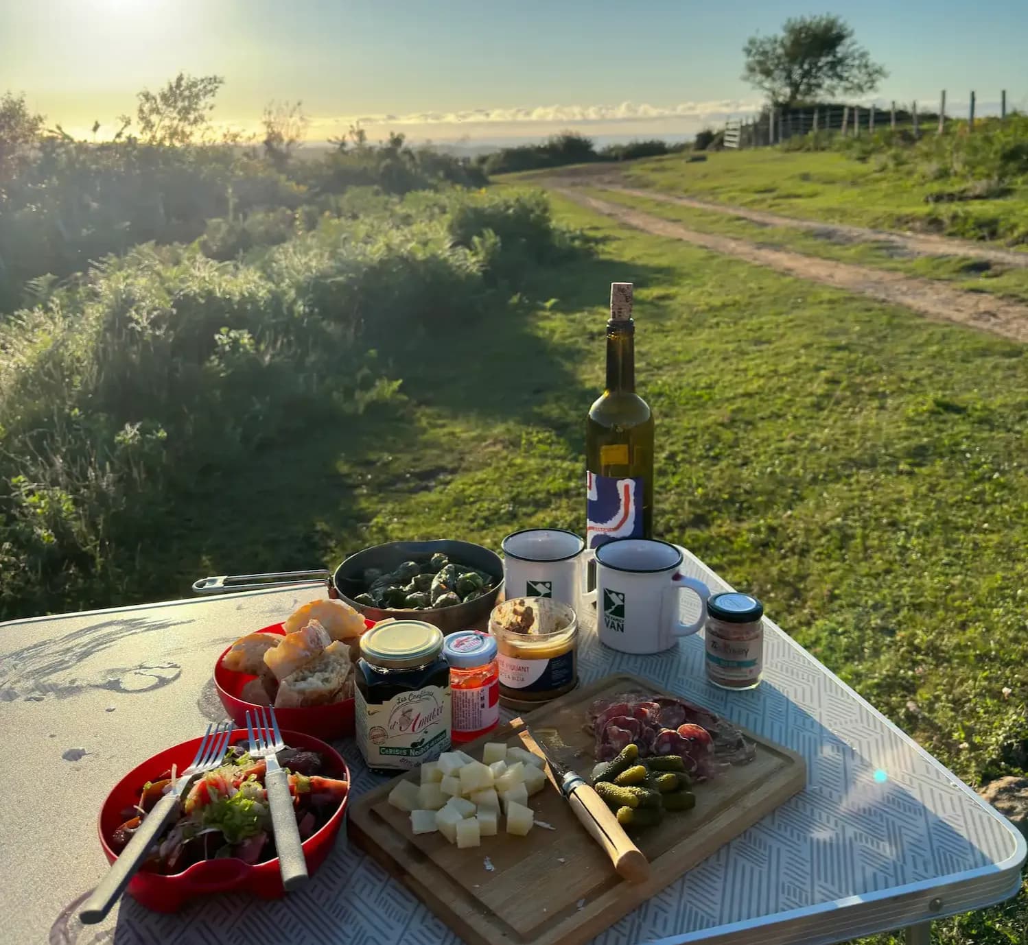 Camping table spread with cheese, charcuterie and white wine looking out over a country track