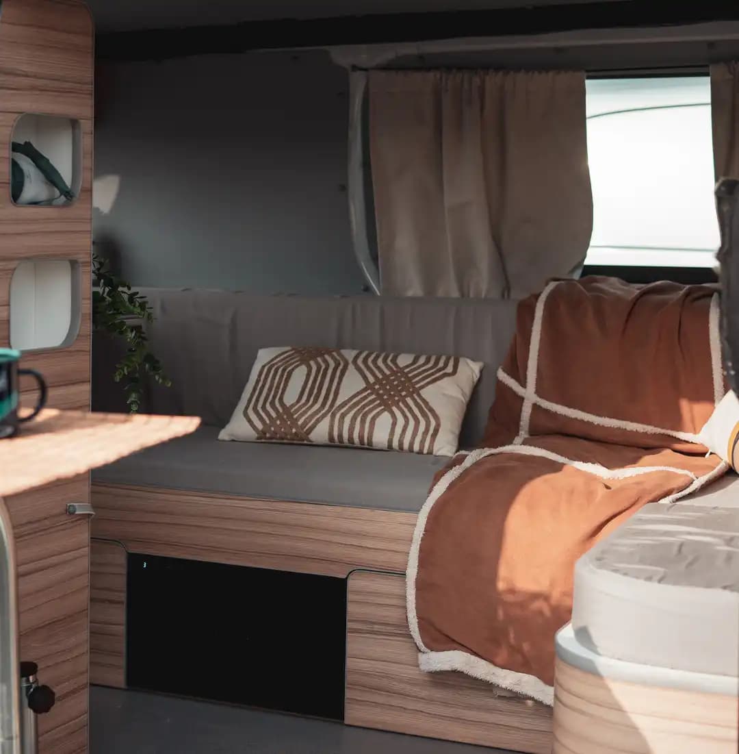 Bench seat inside a campervan with a patterned cushion, terracotta throw and curtains