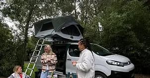 Roof tent open on a campervan, two travellers preparing food beside the open boot